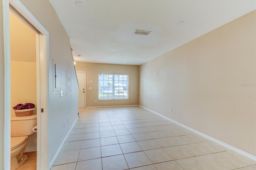 An empty room with beige tile flooring, light walls, and a small bathroom entrance — 509 WILTON CIRCLE, SANFORD, FL
