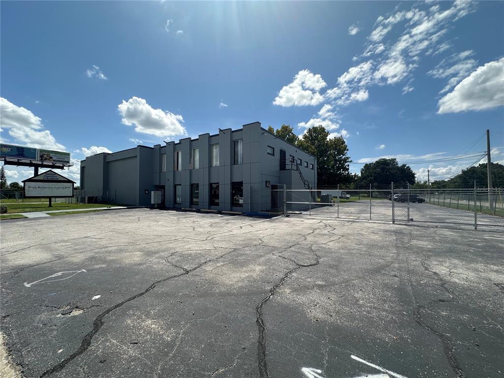 A gray two-story commercial building stands behind a large asphalt parking lot with fencing — 2300 S ORANGE BLOSSOM TRAIL, ORLANDO, FL
