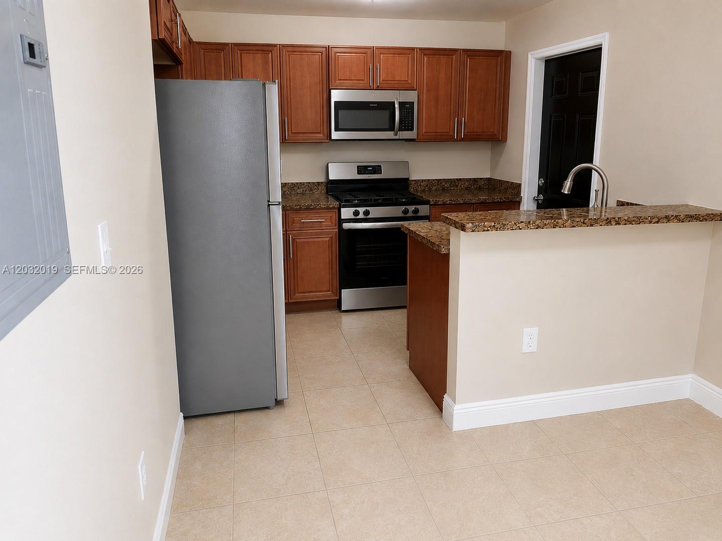 A kitchen features wood cabinets, stainless steel appliances, granite countertops, and tile flooring — 1990 NW 4th Ct # 1, Miami FL 33136, MIAMI, FL