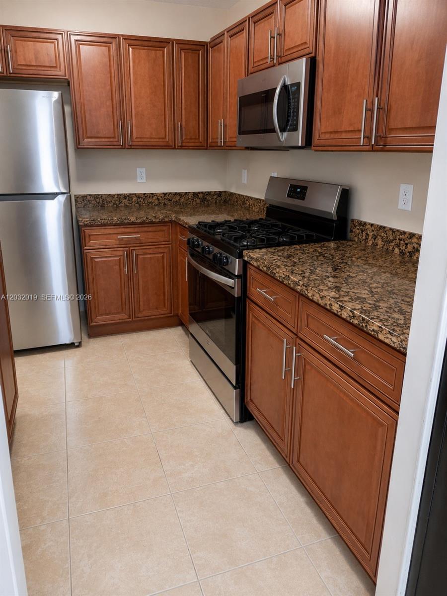 A kitchen features wood cabinets, granite countertops, stainless steel appliances, and light-colored tile flooring — 1990 NW 4th Ct # 1, Miami FL 33136, MIAMI, FL