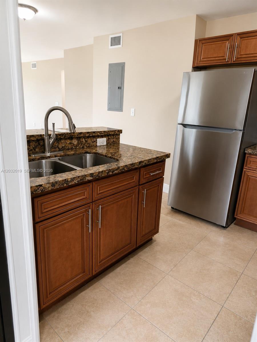 A kitchen features brown wooden cabinets, granite countertops, a stainless steel refrigerator, and tile flooring — 1990 NW 4th Ct # 1, Miami FL 33136, MIAMI, FL
