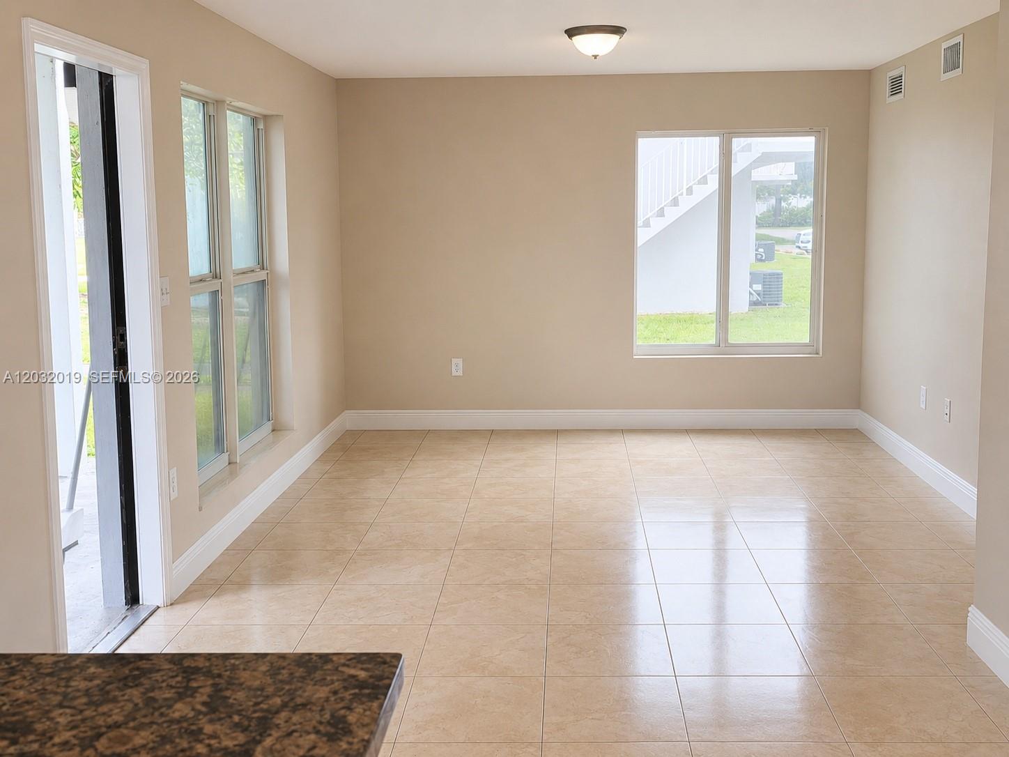 An empty room features beige tile flooring, neutral walls, and windows overlooking an exterior staircase — 1990 NW 4th Ct # 1, Miami FL 33136, MIAMI, FL