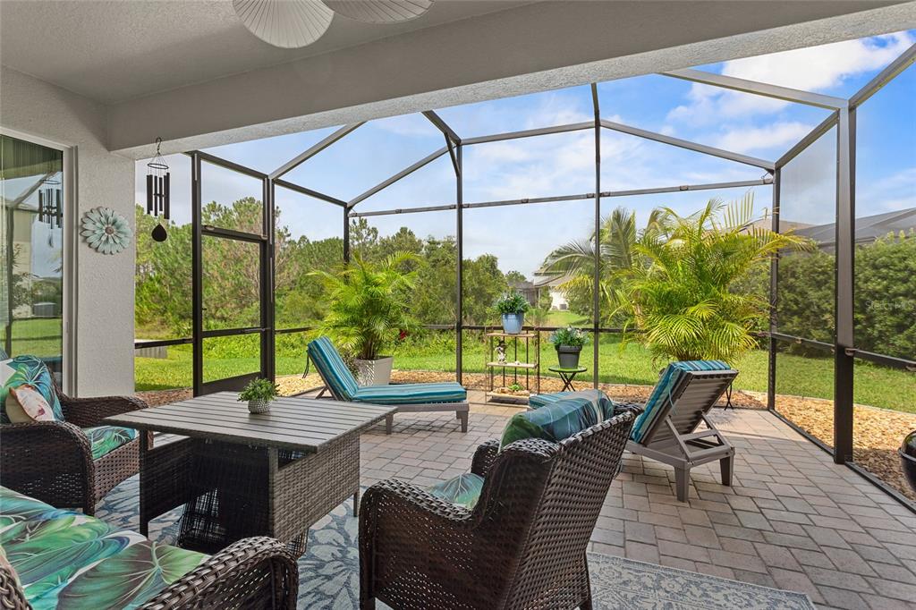 A covered patio with wicker furniture, a dining table, and a screened-in view of greenery — 2215 CAMDEN PARK AVENUE, DAVENPORT, FL