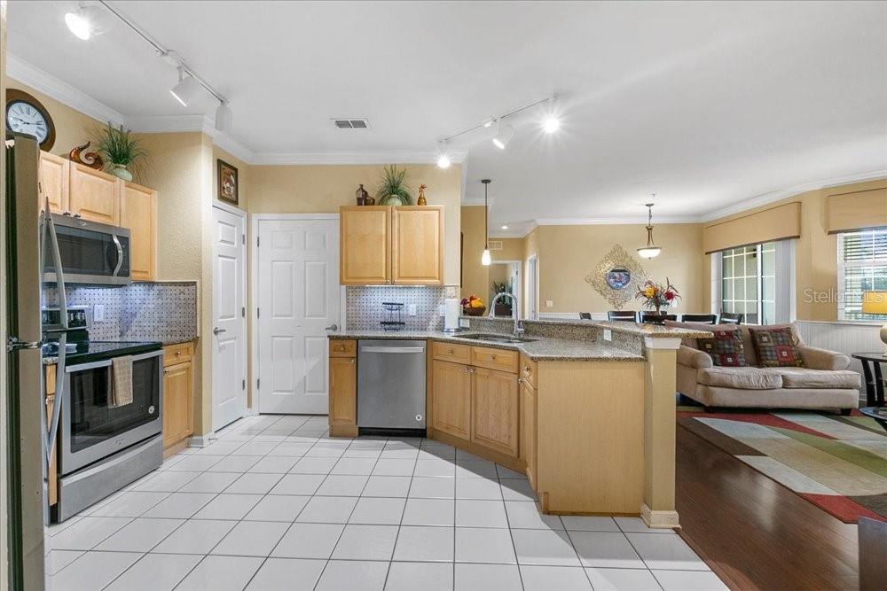 A kitchen with light wood cabinets, granite countertops, and white tile flooring opens to a living area — 110 TERRACE RIDGE CIRCLE UNIT 110, DAVENPORT, FL