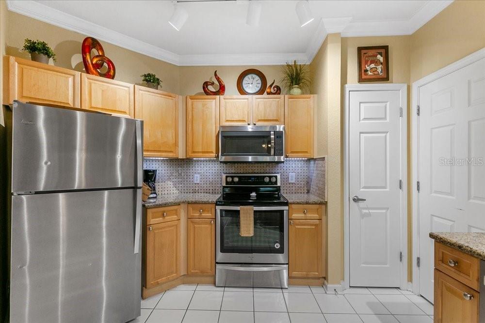 A kitchen features light wood cabinets, stainless steel appliances, a tiled backsplash, and white floor tiles — 110 TERRACE RIDGE CIRCLE UNIT 110, DAVENPORT, FL