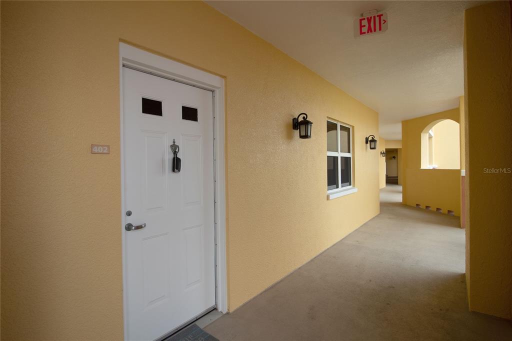 An exterior hallway with yellow walls, a white door labeled 402, and an exit sign — 615 RIVIERA DUNES WAY UNIT 402, PALMETTO, FL