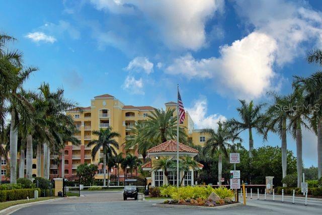 A multi-story yellow residential building stands behind a gated entrance with palm trees — 615 RIVIERA DUNES WAY UNIT 402, PALMETTO, FL