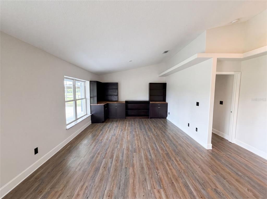 An empty room with wood-look flooring, light walls, and a built-in dark wood desk unit — 2620 KELLY LANE, MALABAR, FL