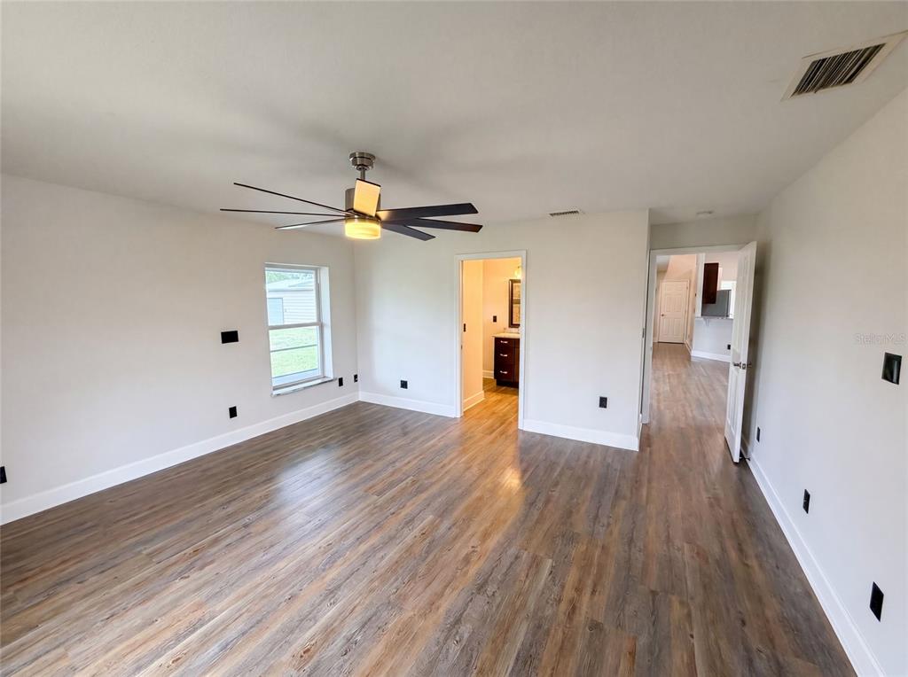 A bedroom with light-colored walls, wood-look flooring, a ceiling fan, and an attached bathroom — 2620 KELLY LANE, MALABAR, FL