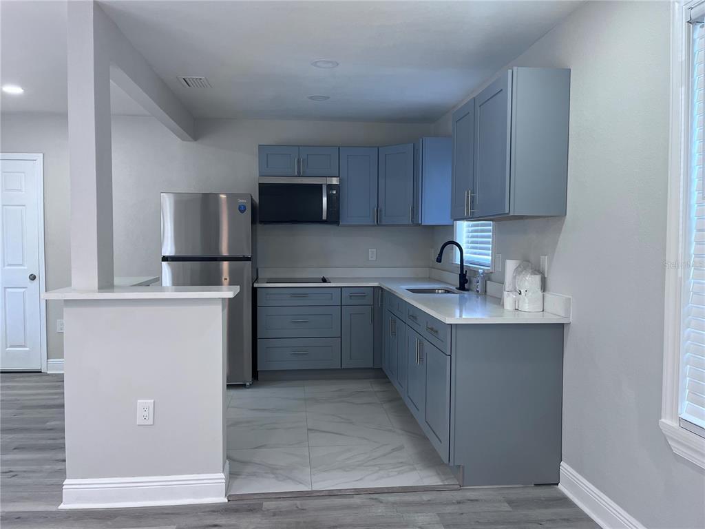 A kitchen features blue cabinets, stainless steel appliances, and white countertops with a tile floor — 3215 W PINE STREET, TAMPA, FL