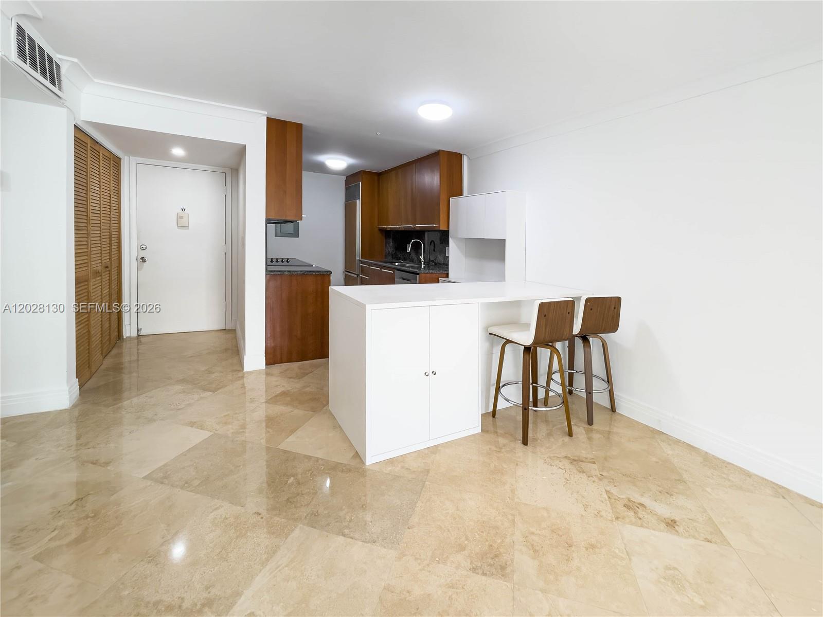 A kitchen features wood cabinets, a white island with two stools, and beige tile floors — 1670 Bay Rd # 2D, Miami Beach FL 33139, MIAMI BEACH, FL