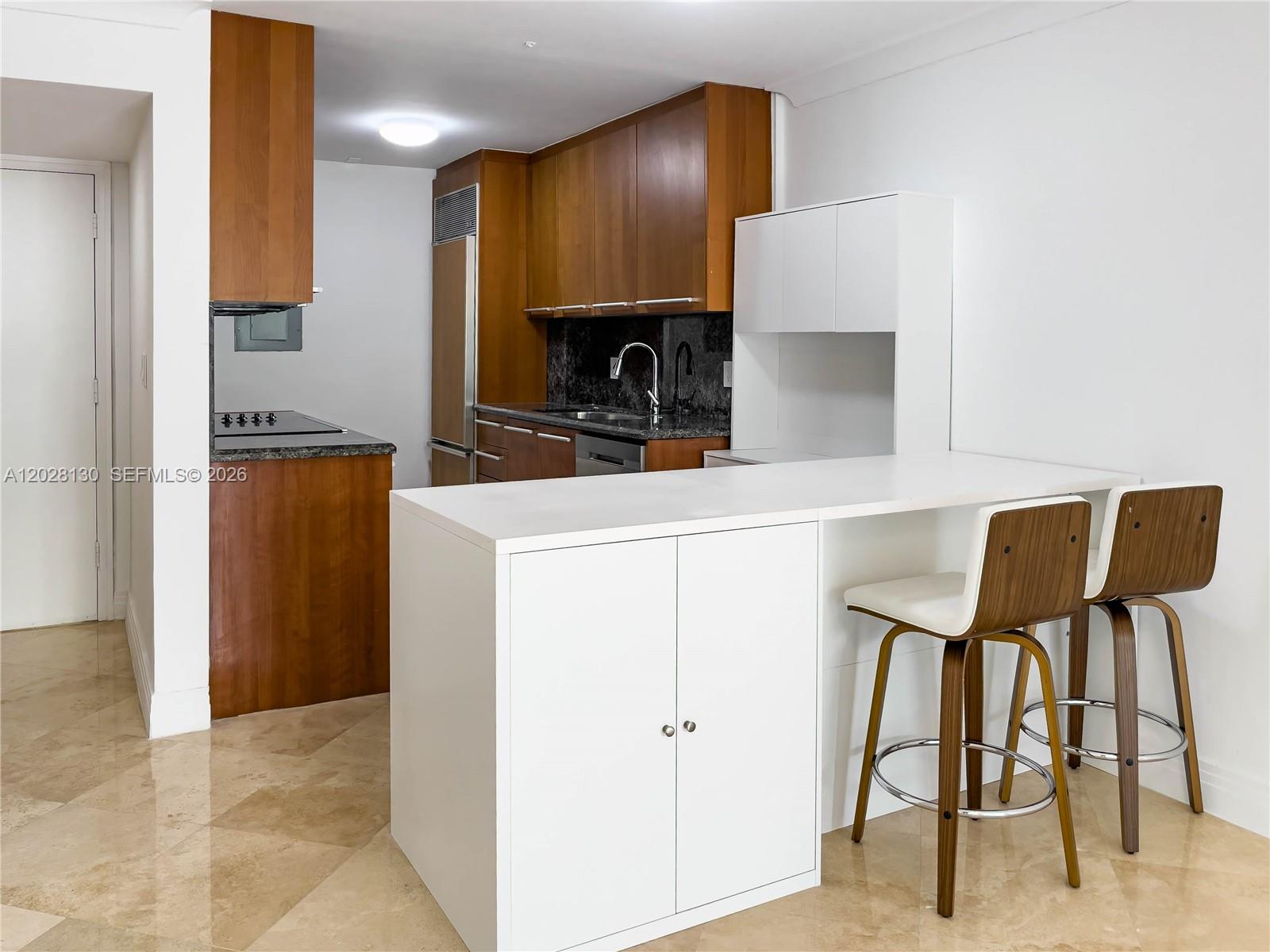 A kitchen features wood cabinets, granite countertops, and a white island with two bar stools — 1670 Bay Rd # 2D, Miami Beach FL 33139, MIAMI BEACH, FL