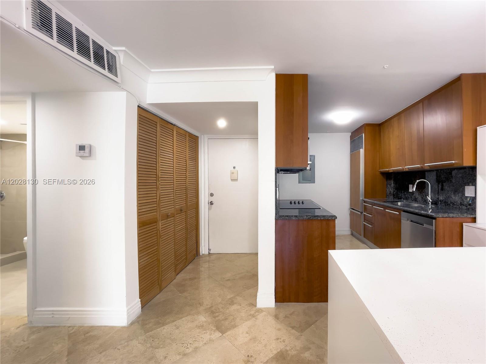 A kitchen with wood cabinets and granite countertops sits next to a tiled entryway — 1670 Bay Rd # 2D, Miami Beach FL 33139, MIAMI BEACH, FL