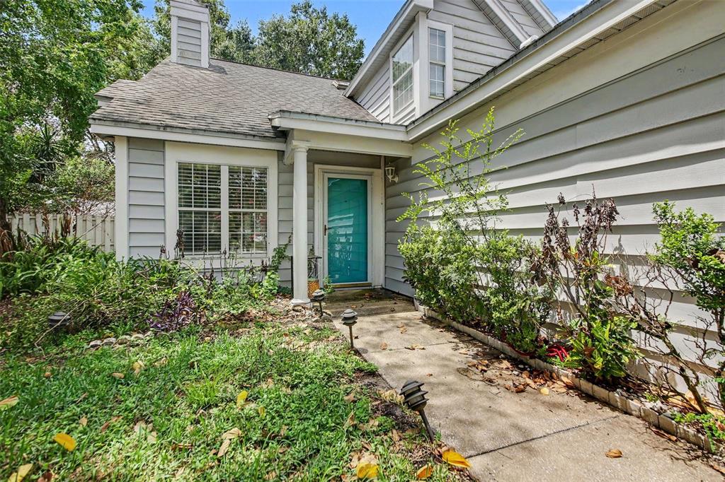 A light gray house features a teal front door, a concrete walkway, and overgrown landscaping — 2758 WAYMEYER DR, ORLANDO, FL