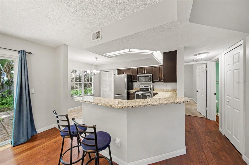 A kitchen with granite countertops, dark cabinets, and stainless steel appliances overlooks a dining area — 2758 WAYMEYER DR, ORLANDO, FL