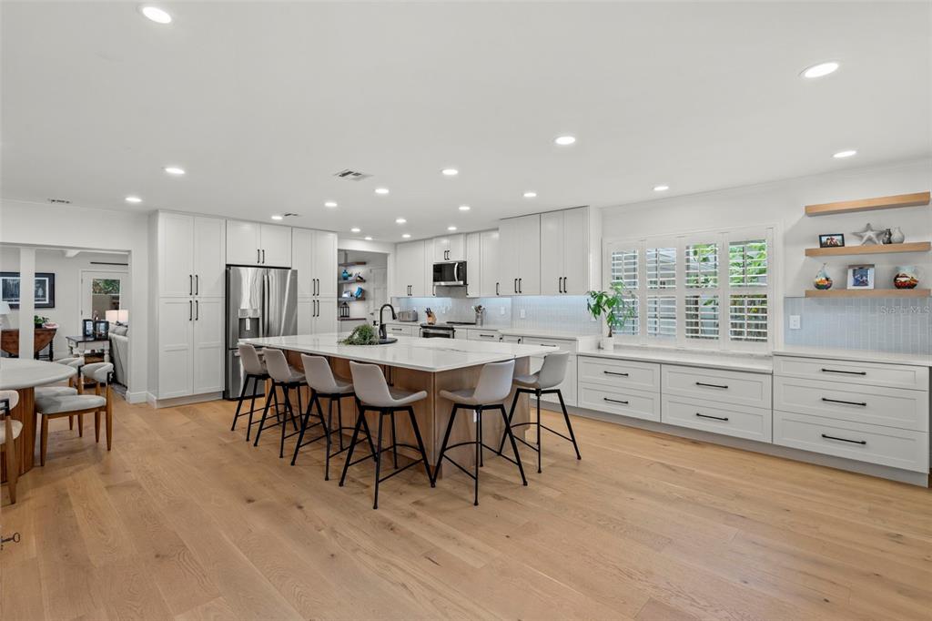 A modern white kitchen features a large island with bar stools and light wood flooring — 480 W DAVIS BOULEVARD, TAMPA, FL