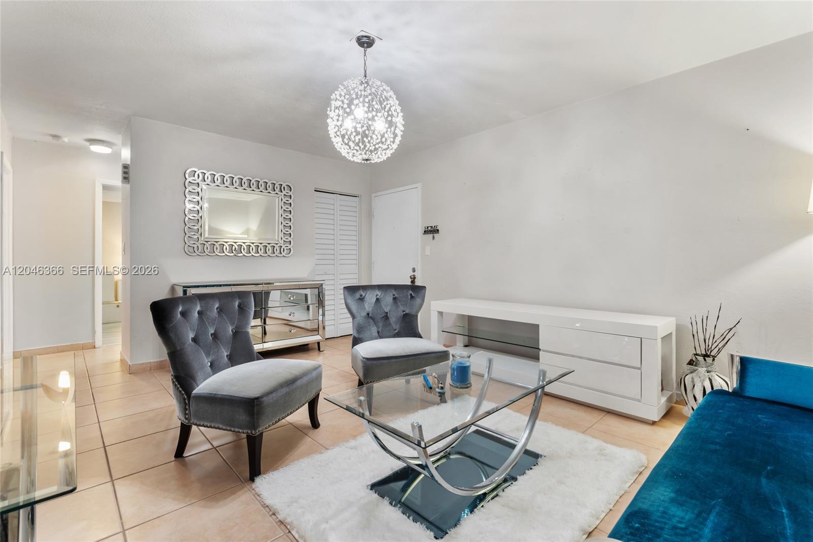 A living room features two grey tufted chairs, a glass coffee table, and a chandelier — 8401 SW 107th Ave # 144E, Miami FL 33173, MIAMI, FL