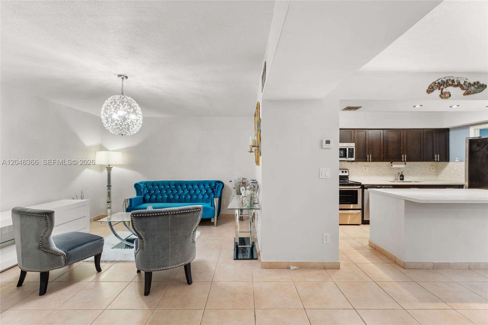 A living room with a blue tufted sofa and two grey chairs leads to a kitchen — 8401 SW 107th Ave # 144E, Miami FL 33173, MIAMI, FL