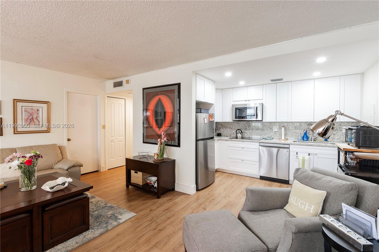 An open-concept living room features wood-look flooring and a white kitchen with stainless appliances — 1440 Brickell Bay Dr # 201, Miami FL 33131, MIAMI, FL