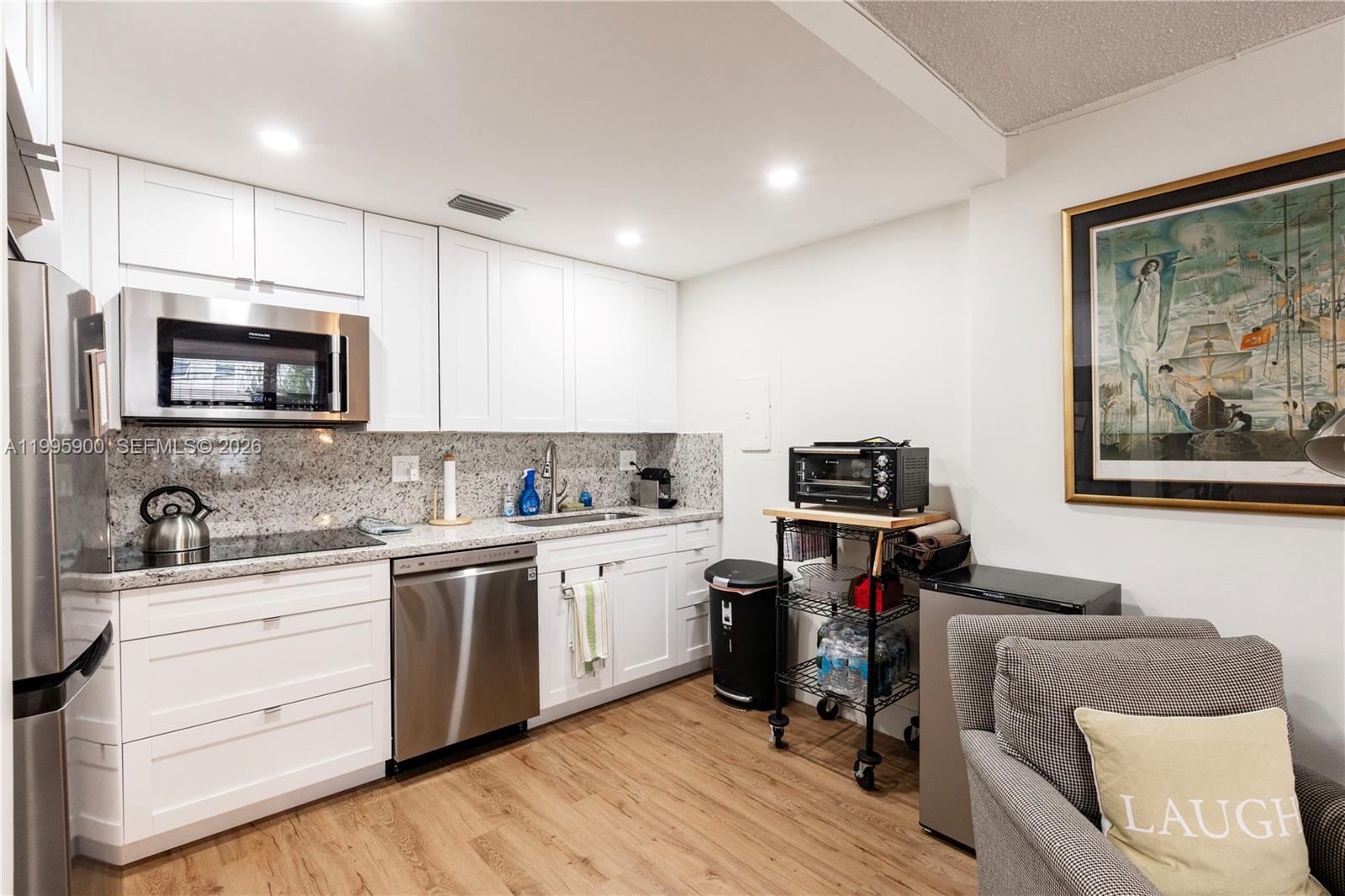 A kitchen features white cabinets, stainless steel appliances, granite countertops, and light wood flooring — 1440 Brickell Bay Dr # 201, Miami FL 33131, MIAMI, FL