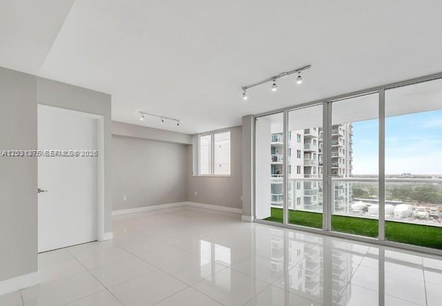 A bright, empty room with white tile floors, track lighting, and a glass balcony door — 1871 NW S River Dr # 1606, Miami FL 33125, MIAMI, FL