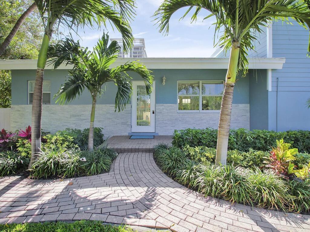 A paved walkway leads to the front entrance of a house with blue siding — 1310 Manor Drive, Singer Island FL 33404, SINGER ISLAND, FL