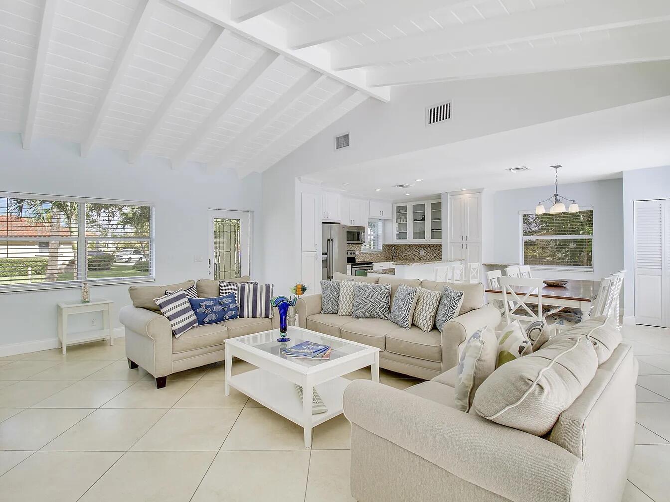 An open-concept living room and kitchen feature vaulted ceilings, tile floors, and neutral furniture — 1310 Manor Drive, Singer Island FL 33404, SINGER ISLAND, FL