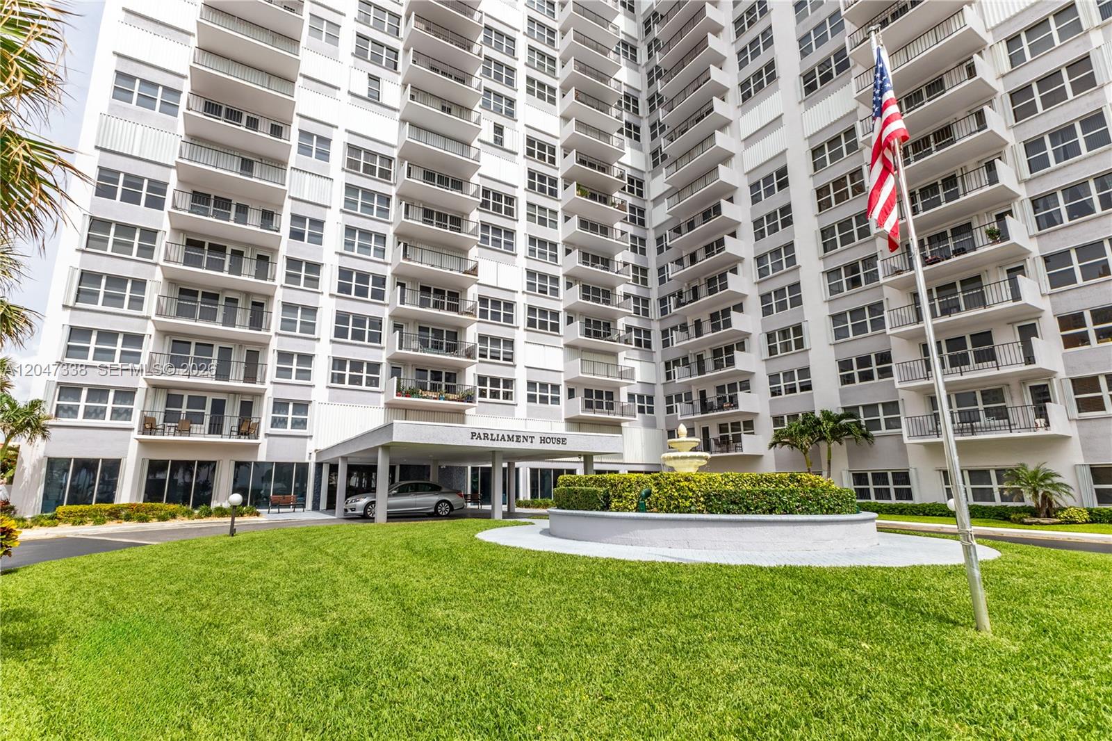 The exterior of a multi-story apartment building features a covered entrance and a front lawn — 405 N Ocean Blvd # 117, Pompano Beach FL 33062, POMPANO BEACH, FL
