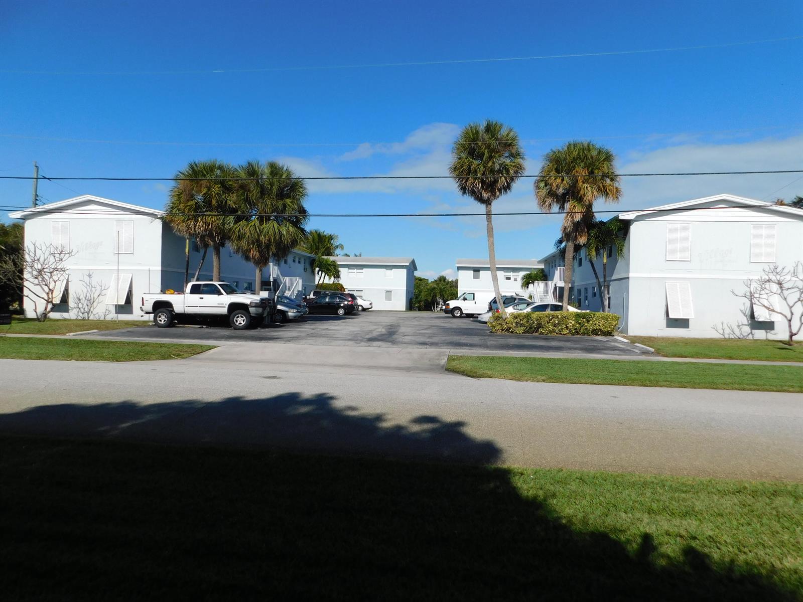 An exterior view of a multi-unit apartment complex with a parking lot and palm trees — 741 Hummingbird Way # 2, North Palm Beach FL 33408, NORTH PALM BEACH, FL