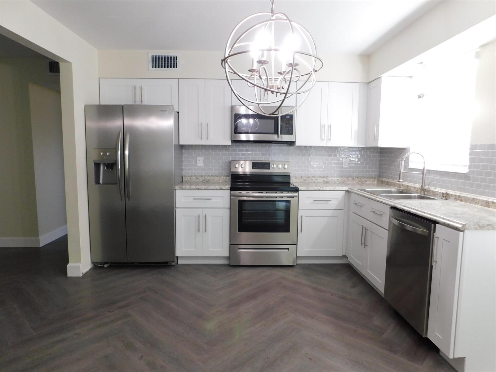 A kitchen features white cabinets, stainless steel appliances, a gray subway tile backsplash, and herringbone flooring — 741 Hummingbird Way # 2, North Palm Beach FL 33408, NORTH PALM BEACH, FL