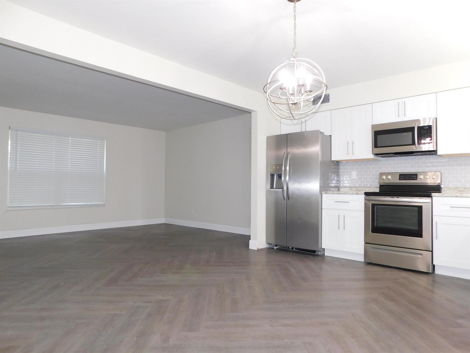 A kitchen with stainless steel appliances and white cabinets opens into an empty living area — 741 Hummingbird Way # 2, North Palm Beach FL 33408, NORTH PALM BEACH, FL