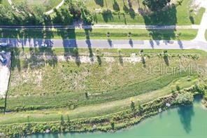 An aerial view shows a vacant, grassy lot situated between a paved road and a pond — 13061 SWINNEY LANE, CLERMONT, FL
