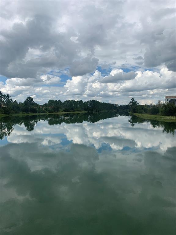 A calm lake reflects a cloudy sky with trees lining the distant shore — 13061 SWINNEY LANE, CLERMONT, FL