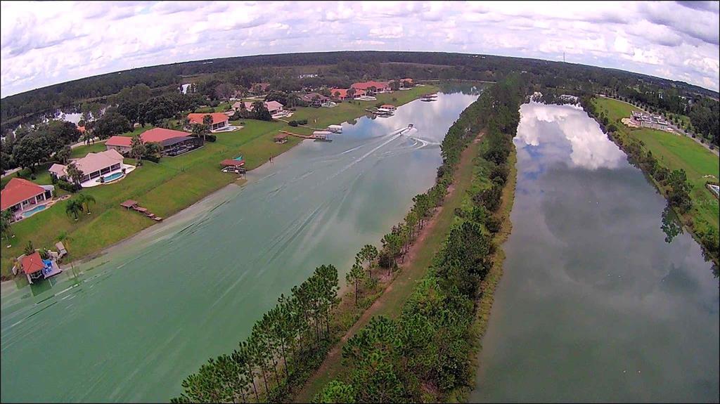 An aerial view shows a residential canal with houses, boat docks, and a boat moving along — 13061 SWINNEY LANE, CLERMONT, FL
