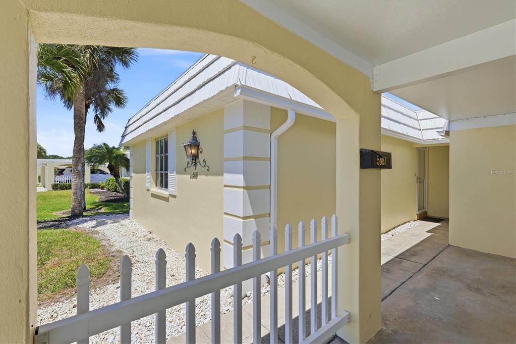 A yellow exterior wall with a white fence and a covered walkway under a roof — 5887 TIDEWOOD AVENUE UNIT 2, SARASOTA, FL