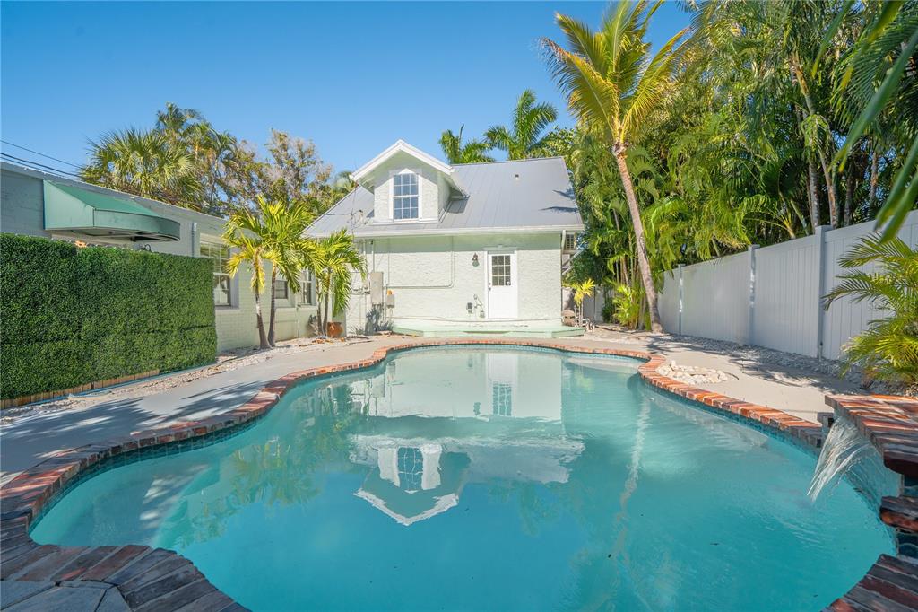 A backyard swimming pool sits in front of a light-colored house with a metal roof — 3310 E MARITANA DRIVE, ST PETE BEACH, FL