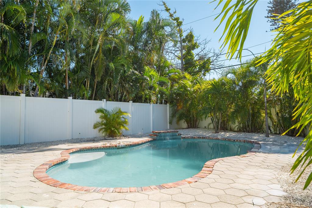 A backyard swimming pool with a brick border, a small waterfall, and a white fence — 3310 E MARITANA DRIVE, ST PETE BEACH, FL