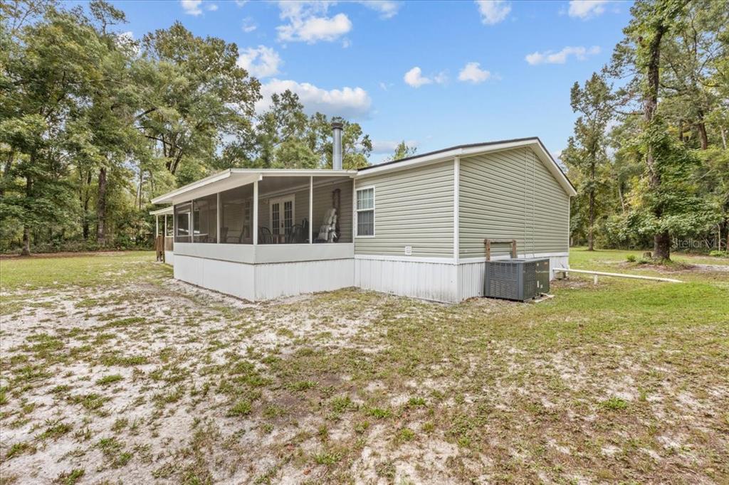 A light green mobile home with a screened-in porch sits on a sandy, wooded lot — 1549 NE 642ND STREET, OLD TOWN, FL