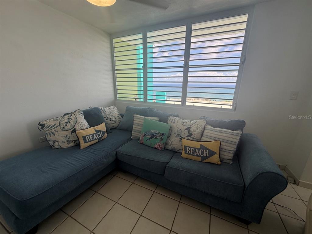A blue sectional sofa sits in a room with tiled floors and ocean-view louvered windows — 471 CALLE 22 BO. MARIANI, MAUNABO, PR