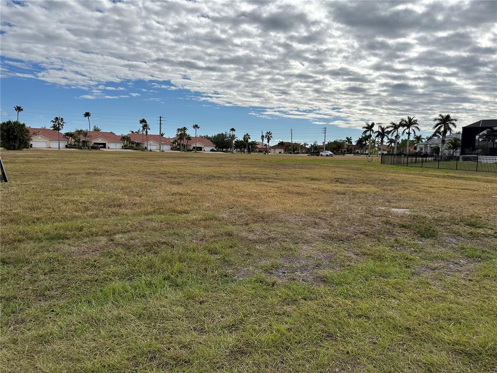 A large, flat, grassy vacant lot with palm trees and houses in the background — 3560 MONDOVI COURT, PUNTA GORDA, FL