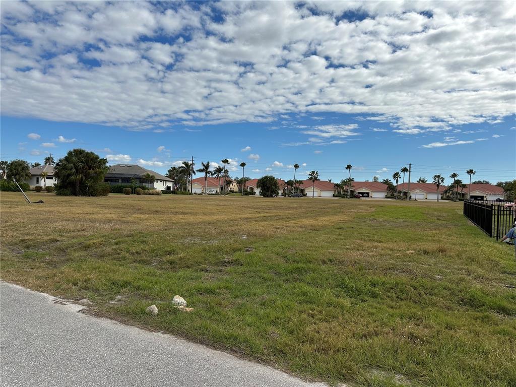 A large, grassy vacant lot sits in front of a row of suburban houses — 3560 MONDOVI COURT, PUNTA GORDA, FL