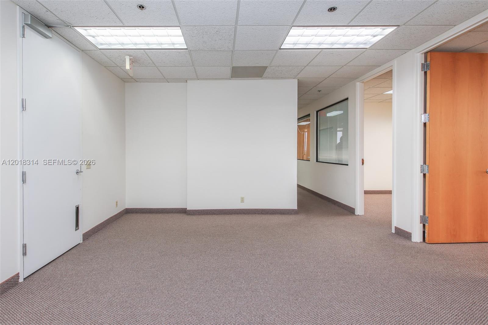 An empty office space features beige carpet, white walls, a wood door, and drop ceilings — 1900 Glades Rd # 430, Boca Raton FL 33431, BOCA RATON, FL