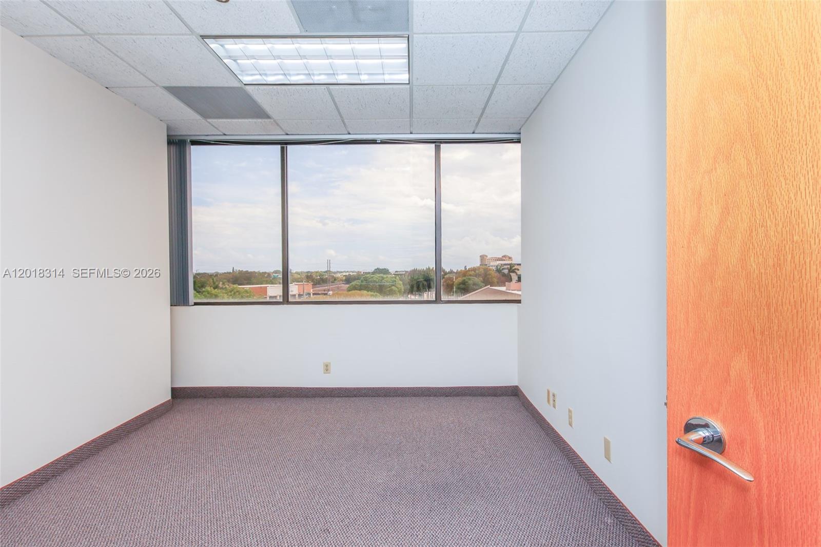 An empty office features gray carpet, white walls, a drop ceiling, and a large window — 1900 Glades Rd # 430, Boca Raton FL 33431, BOCA RATON, FL
