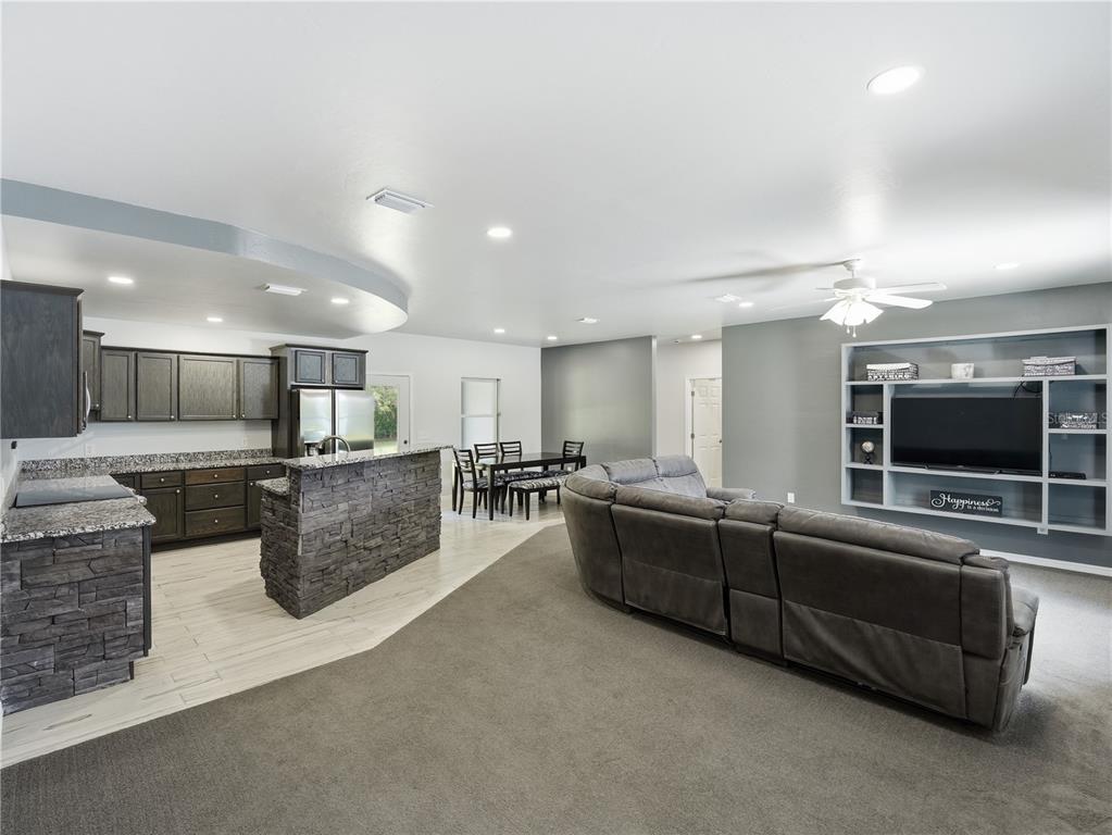 An open-concept living room and kitchen featuring dark cabinetry, stone-faced counters, and gray carpeting — 450 ROSEDALE AVENUE, ST CLOUD, FL