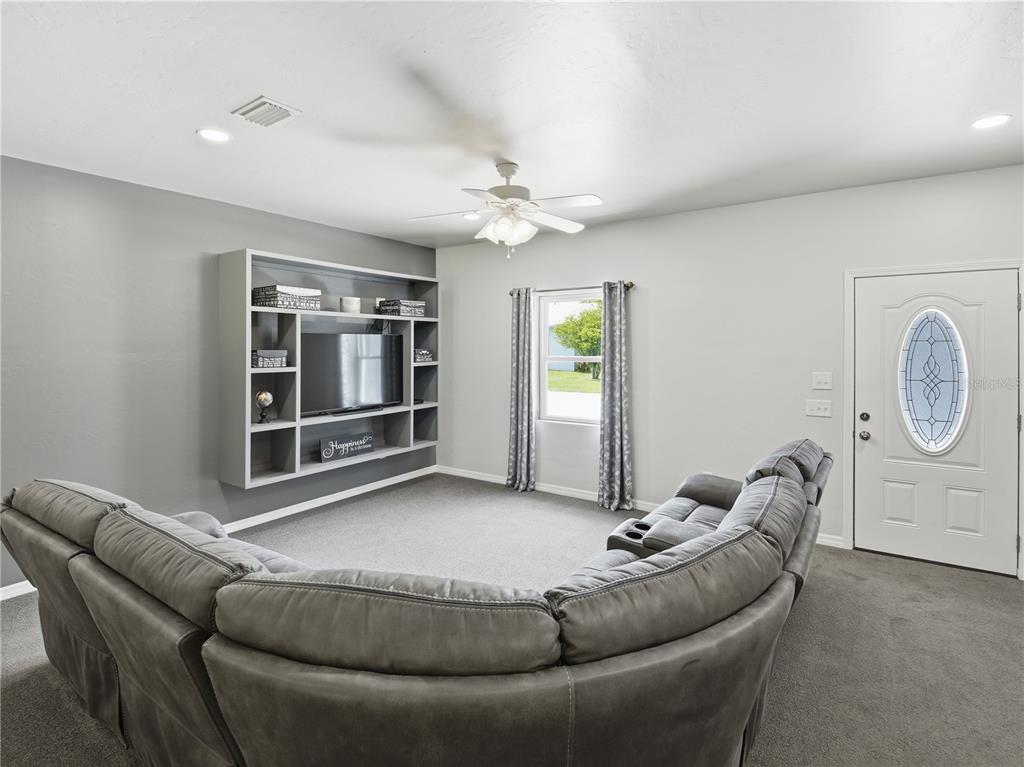 A living room features a large gray sectional sofa, a built-in media center, and carpeted flooring — 450 ROSEDALE AVENUE, ST CLOUD, FL