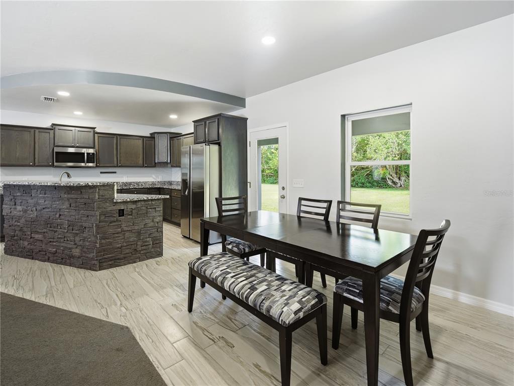 A kitchen with dark cabinets and stone veneer island opens to a dining area — 450 ROSEDALE AVENUE, ST CLOUD, FL