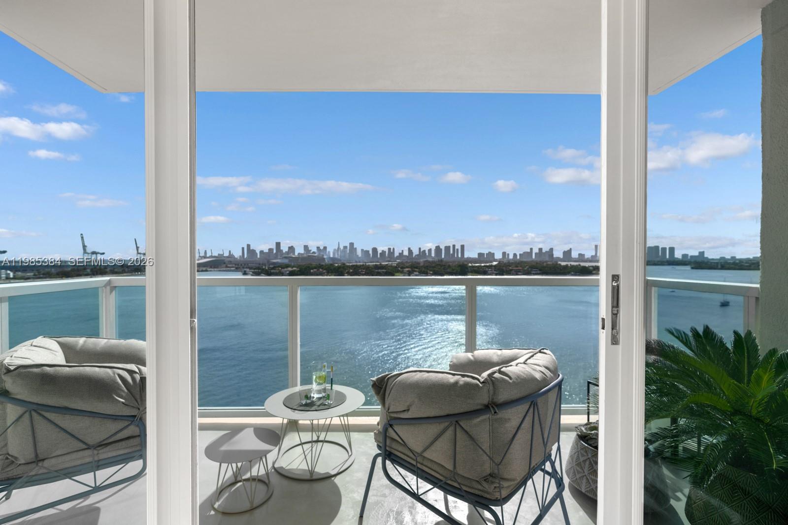 A balcony with two chairs and a small table overlooks a bay and city skyline — 650 West Ave, Miami Beach FL 33139, MIAMI BEACH, FL