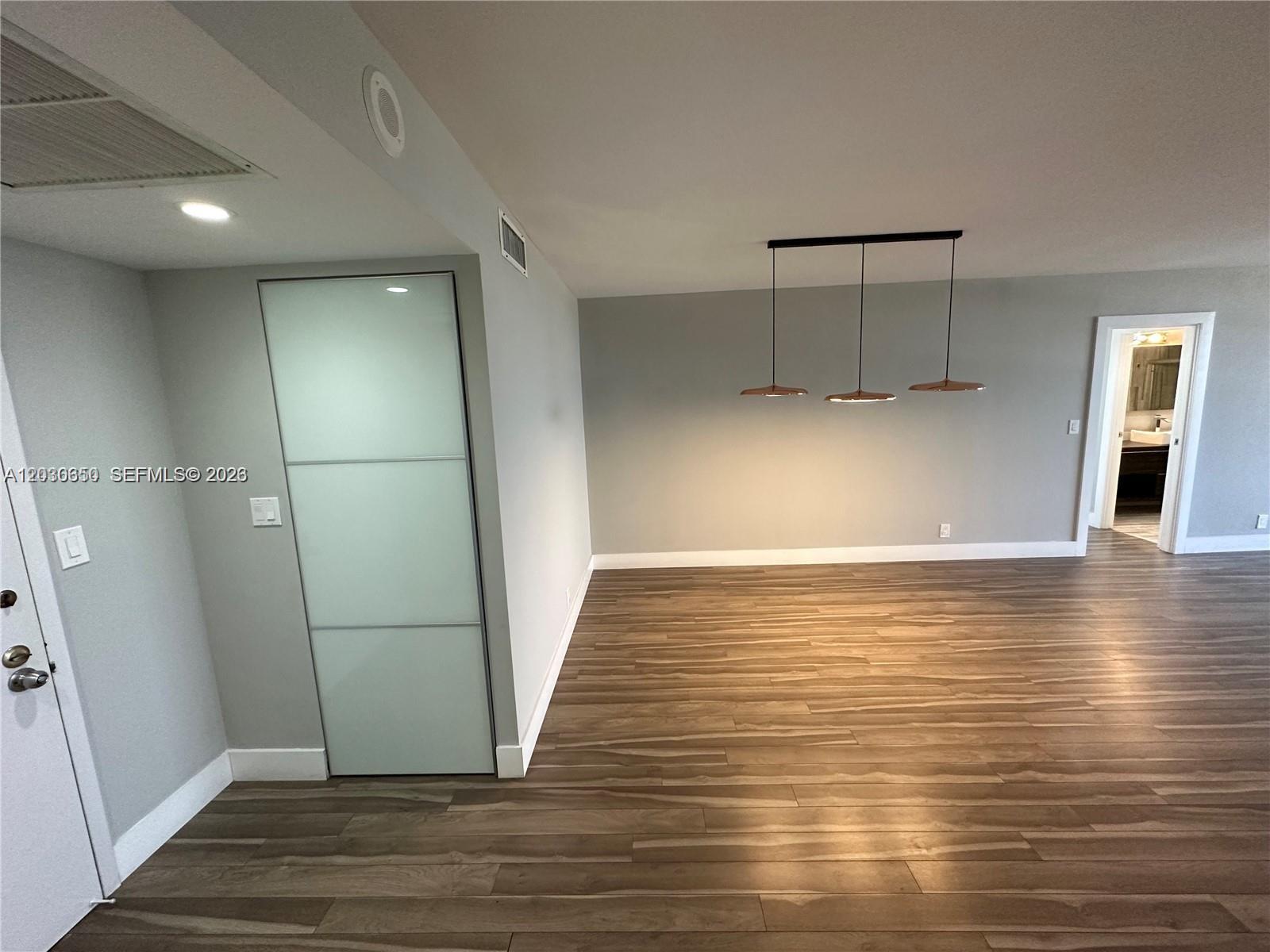 A room with wood-look flooring, a frosted glass door, and a three-light pendant fixture — 600 Three Islands Blvd # 705, Hallandale Beach FL 33009, HALLANDALE BEACH, FL