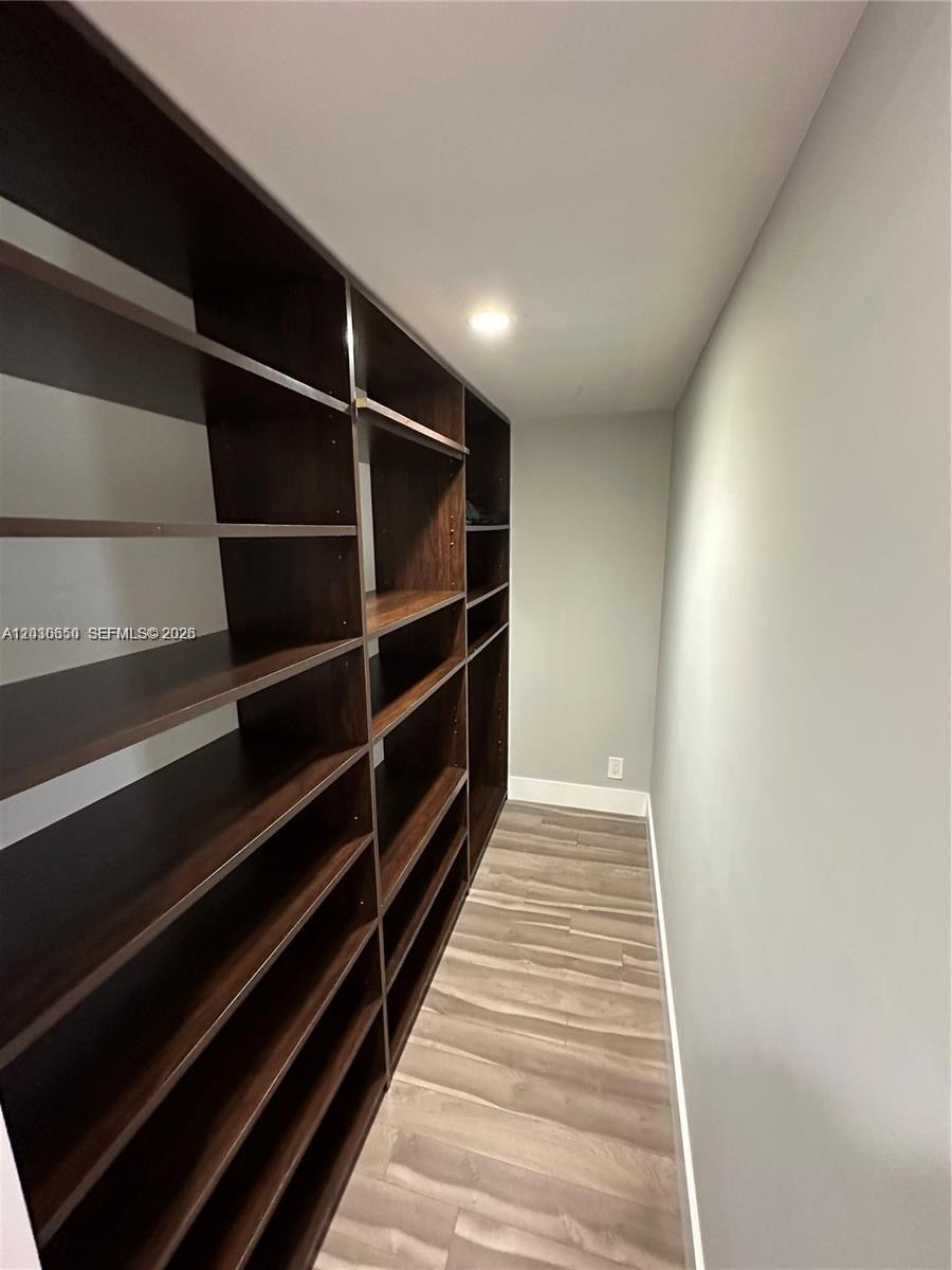 A walk-in closet features dark wood shelving units against a light gray wall — 600 Three Islands Blvd # 705, Hallandale Beach FL 33009, HALLANDALE BEACH, FL