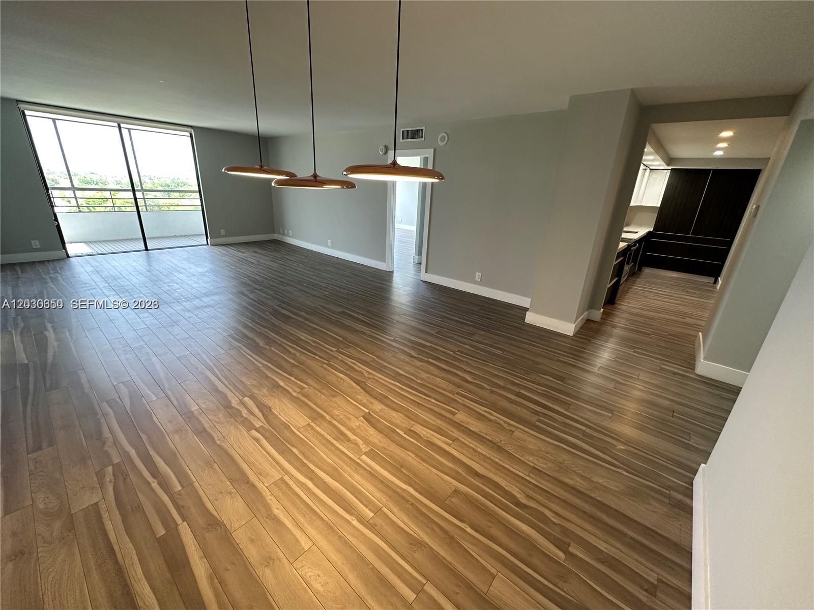 An open-concept living area features wood-look flooring, three pendant lights, and a balcony entrance — 600 Three Islands Blvd # 705, Hallandale Beach FL 33009, HALLANDALE BEACH, FL